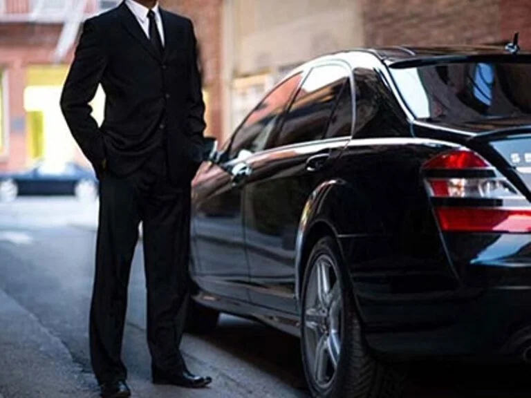 A man in a suit standing next to a black car.