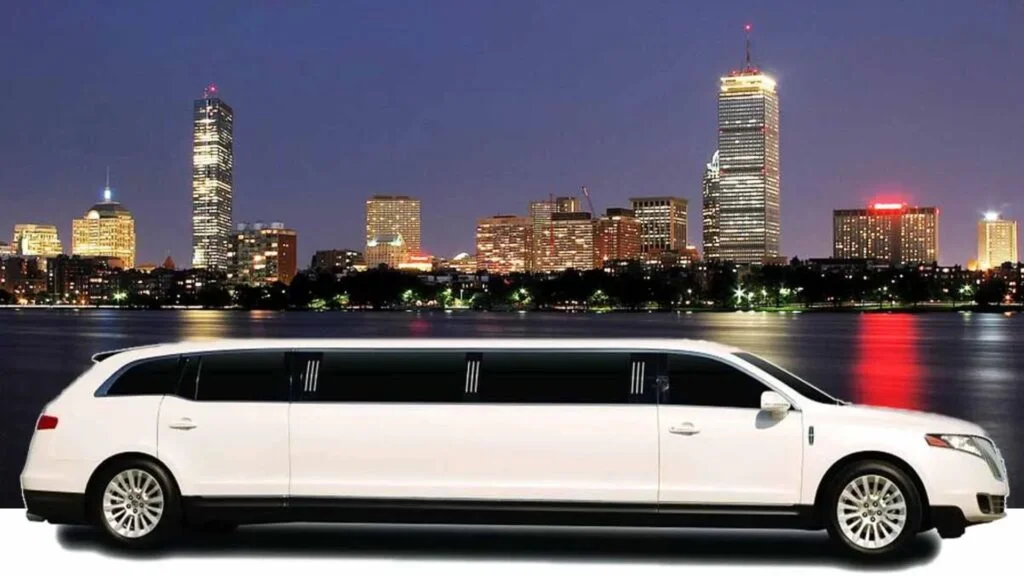 A white limo driving down the street in front of some buildings.