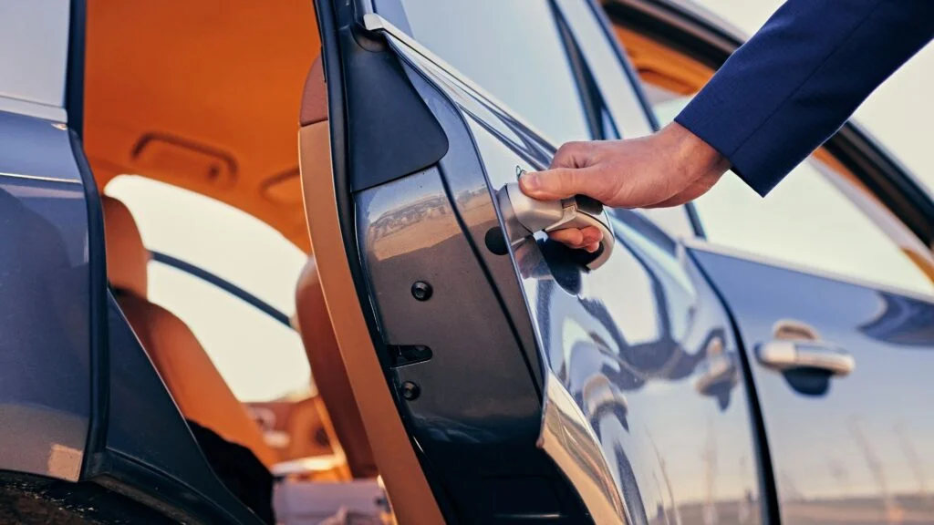 A person is holding the door handle of a car.