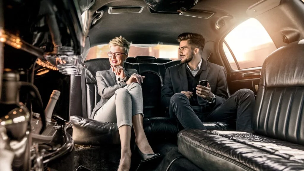 Two people sitting in a limo with their cellphones.