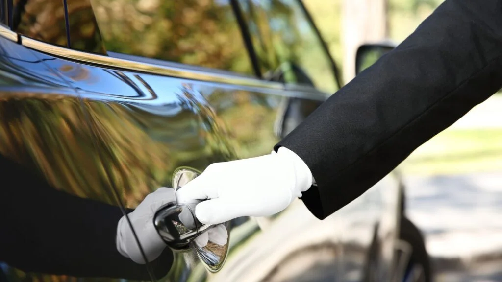 A person in white gloves opening the door of a car.