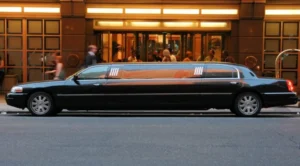 A black car driving down the street with people walking by.