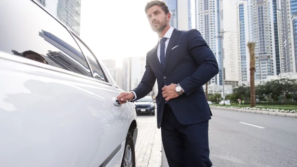 A man in a suit and tie standing next to a car.