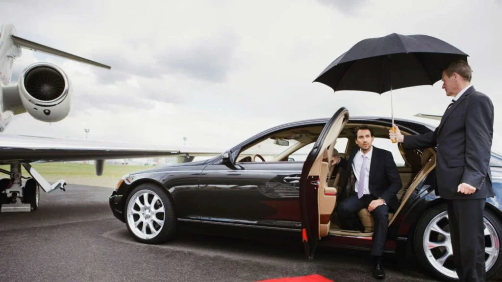 A man sitting in the driver 's seat of a car with an umbrella over him.