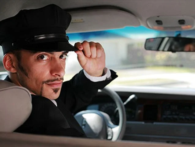 A man in a hat and suit driving a car.