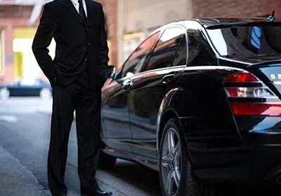 A man in a suit standing next to a black car.