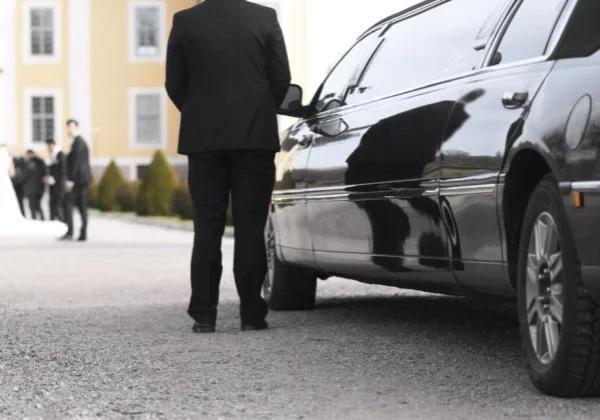 A man in black suit standing next to a silver car.