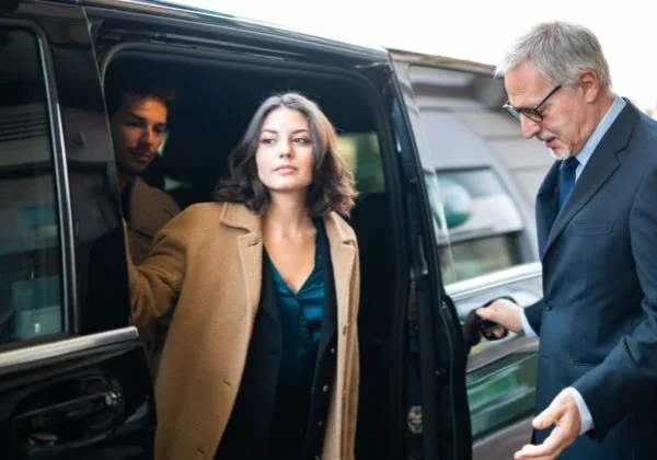 A woman in a brown coat is getting out of the car