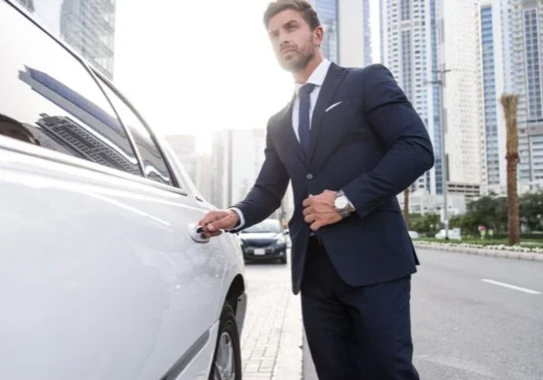 A man in a suit and tie standing next to a car.