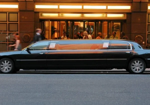 A black car driving down the street with people walking by.