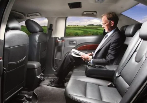 A man sitting in the back of a car reading.