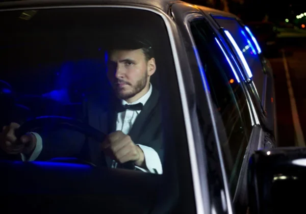 A man in a tuxedo driving a car at night.