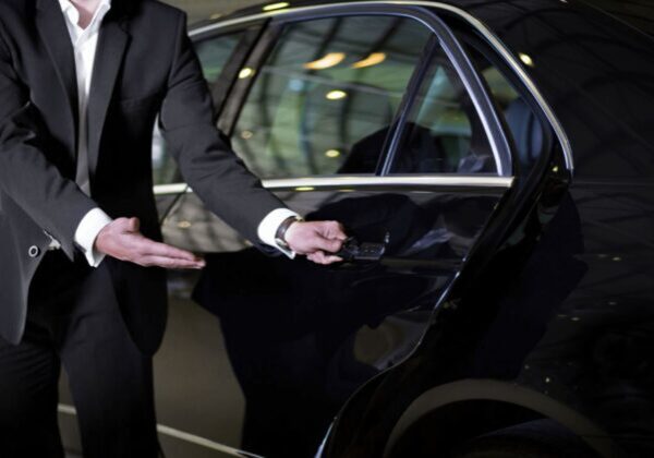 A man in black suit standing next to a car.