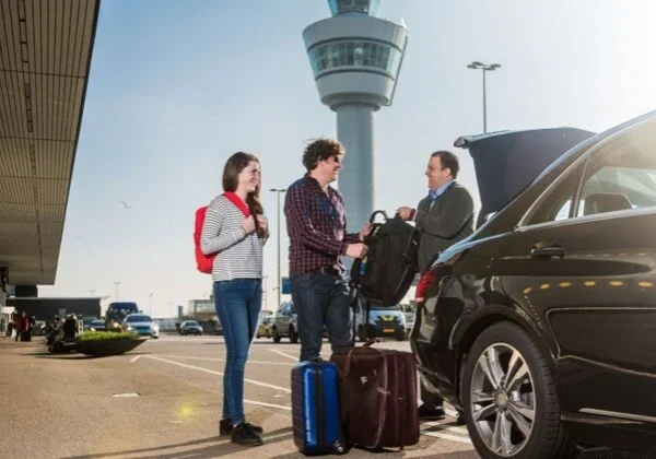 Three people standing next to a car with luggage.