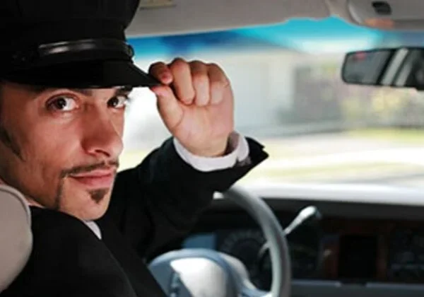 A man in a hat and suit driving a car.